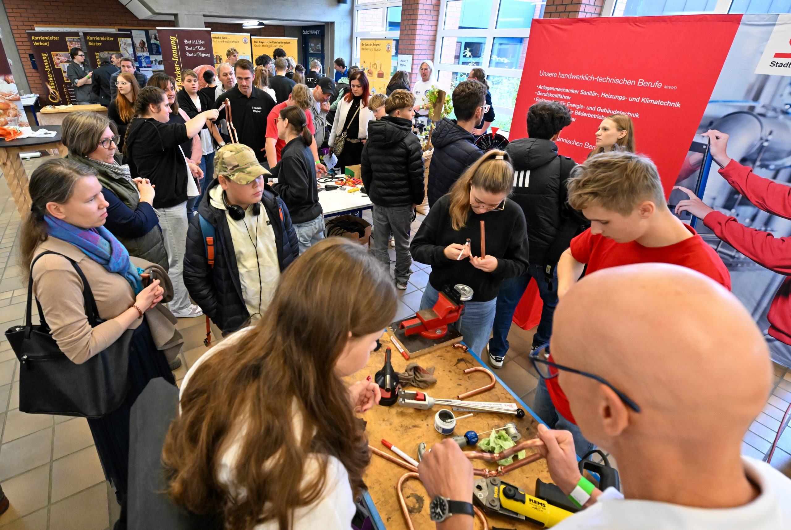 Jugendliche stehen um einen Stand herum und fertigen Metallherzen aus Kupfer.