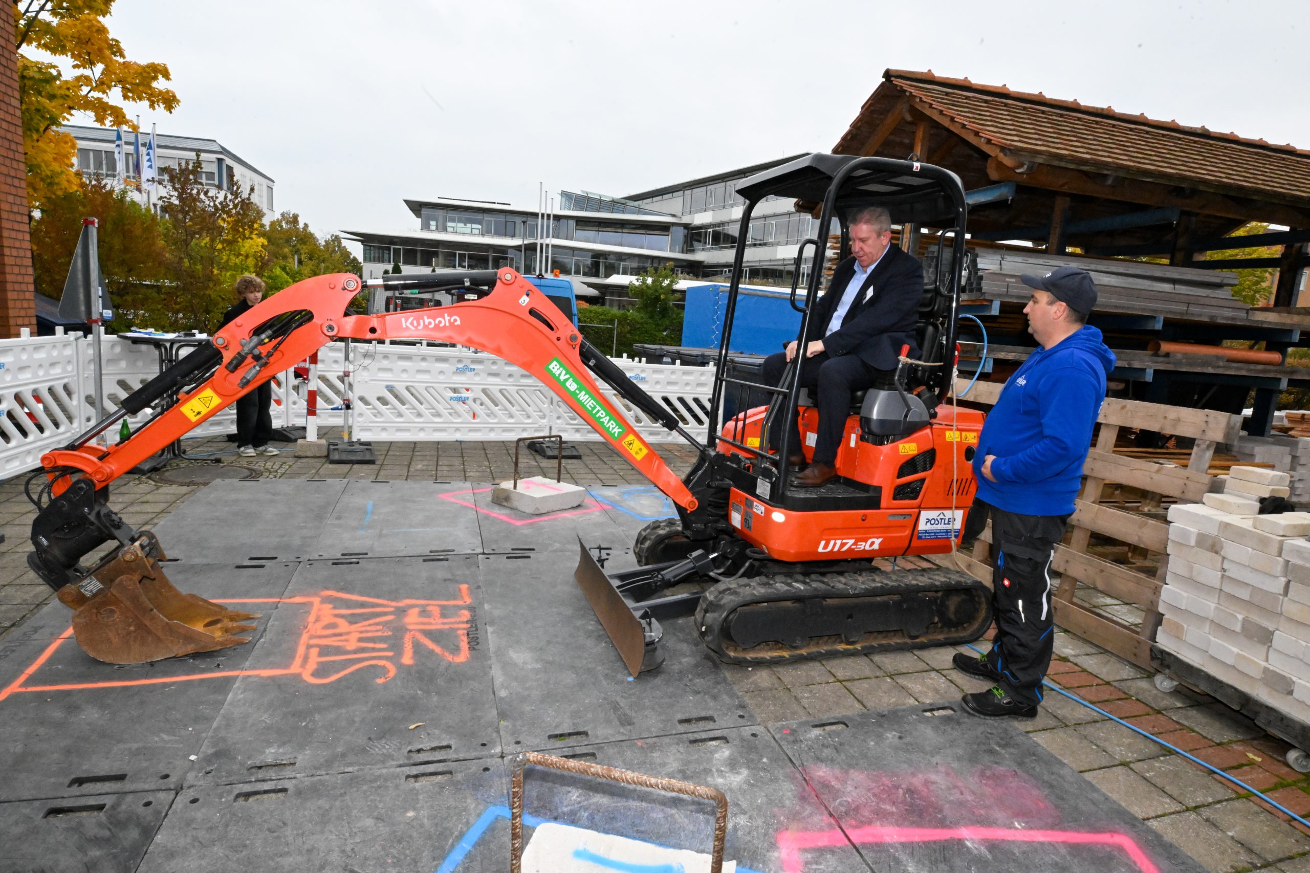 Ein Mann fährt unter Anleitung mit einem Bagger und bedient die Schaufel.