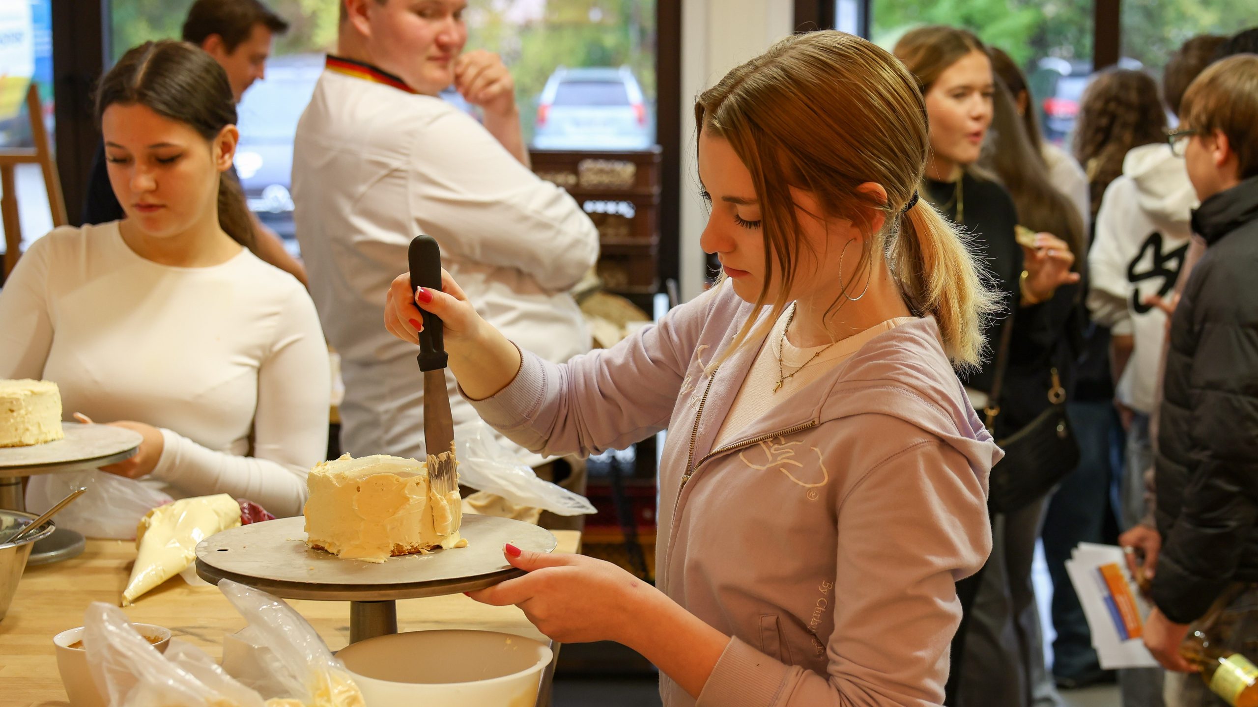 Eine Jugendliche spachelt Buttercreme auf einen Tortenteig.