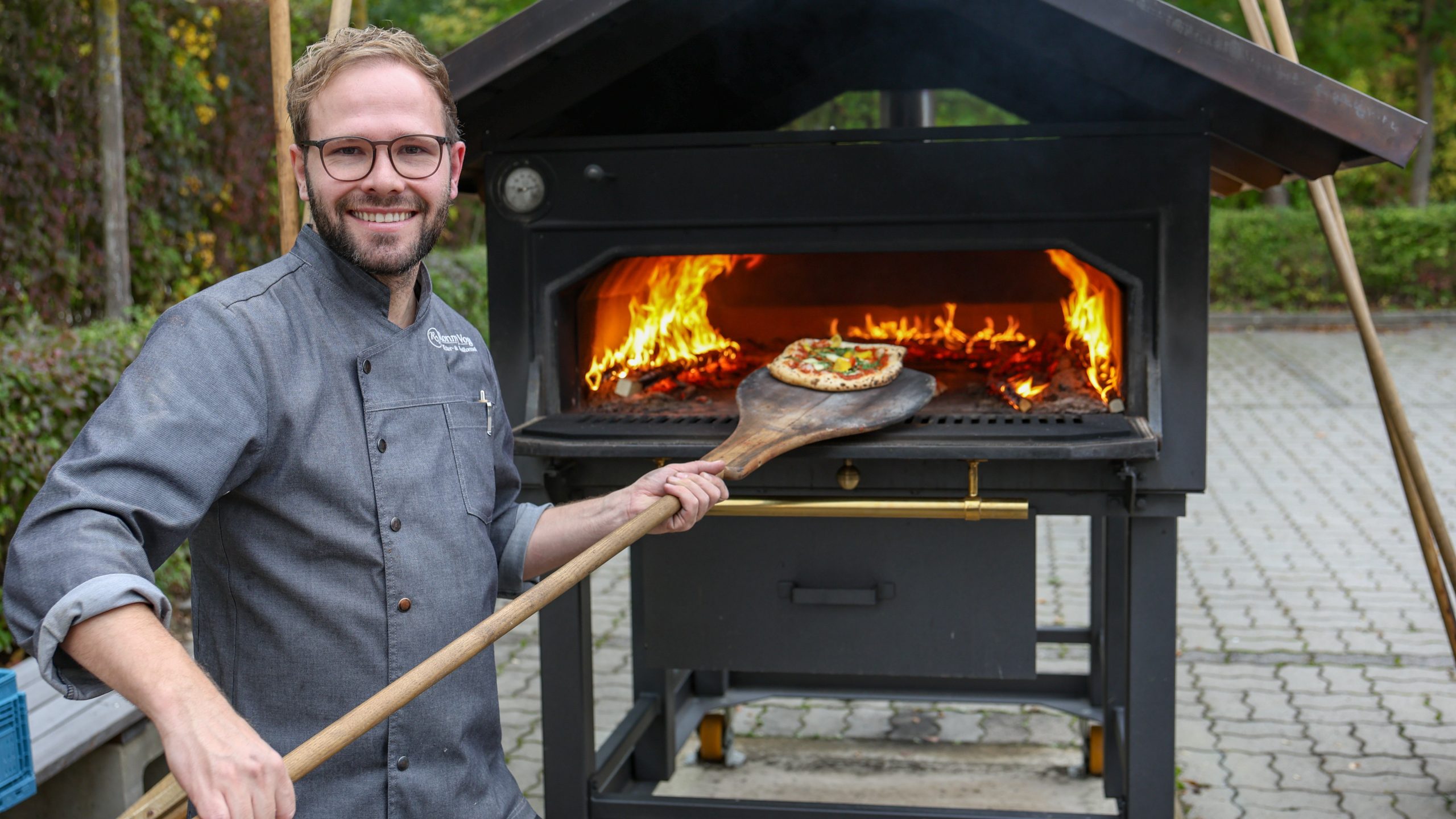 Ein Mann schiebt eine Pizza in einen Holzofen.