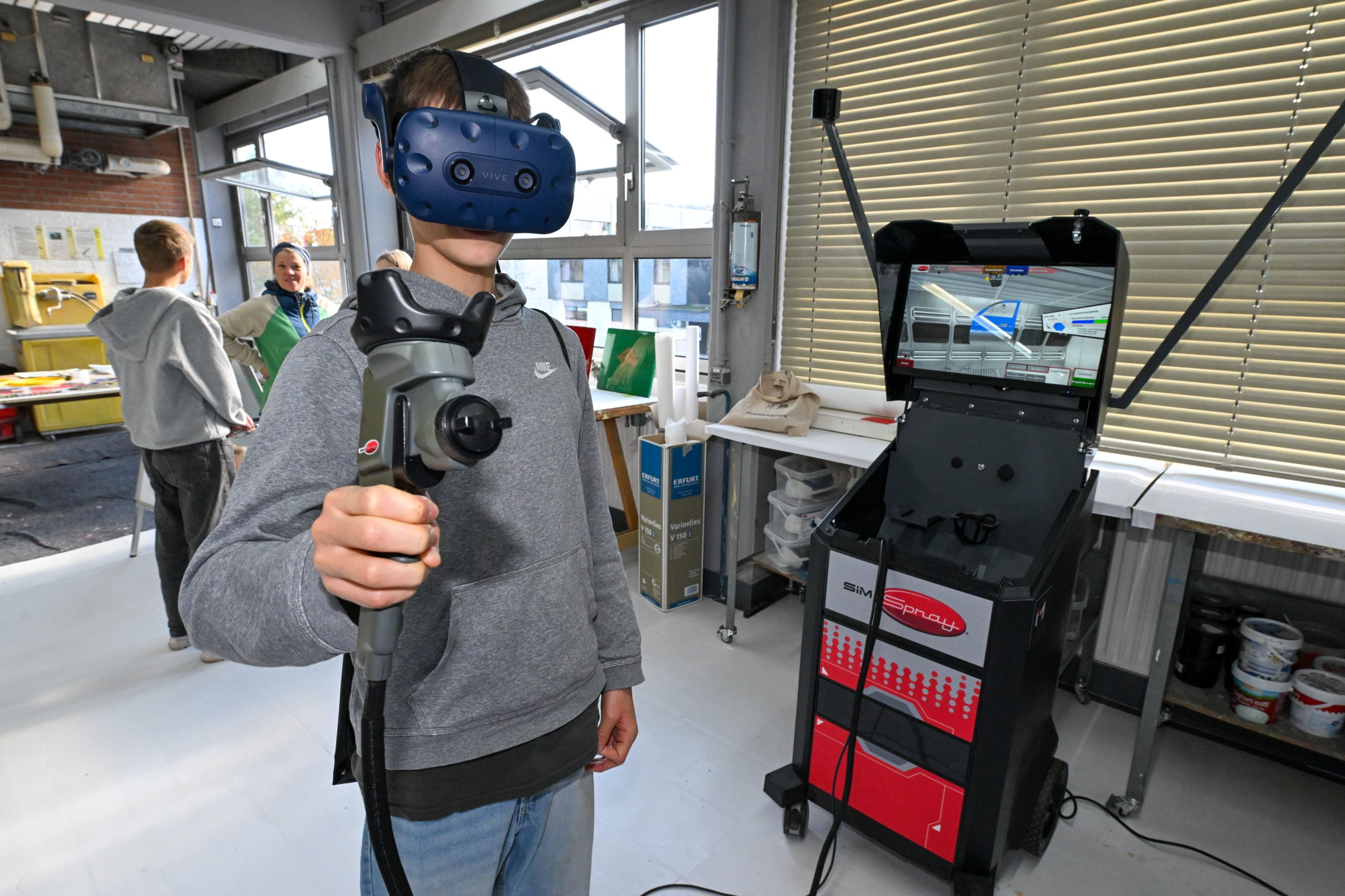 Ein Jugendlicher trägt eine VR-Brille und eine Spritzpistole und lackiert virtuell eine Autotür.